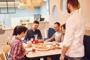 Chef delivers food. Group of young friends who are eating out in Romanian, that sitting together indoors.
