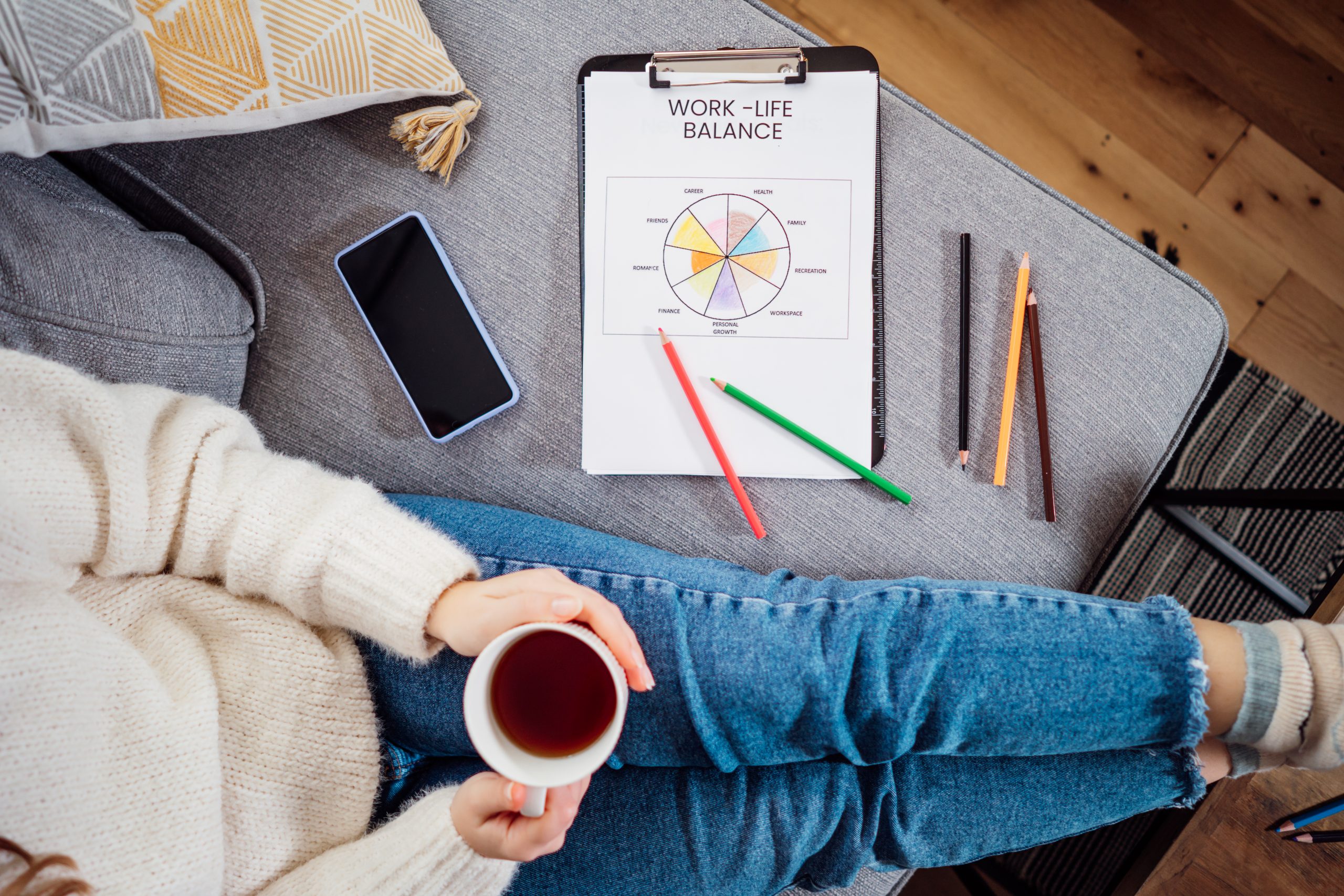Top view of woman relaxing, who learn Romanian time expressions, drinking tea after drawing work-life balance wheel sitting on the sofa at home. Self-reflection and life planning. Coaching tools. Finding Balance in Life. Selective focus.