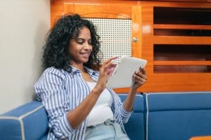 Ethnic woman studying on tablet Romanian A2 imperfect tense while sitting on the sofa
