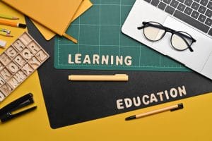 Flat lay laptop computer mentioning Romanian Lessons A2 review grammar, , eyeglasses and stationery on yellow